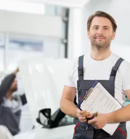Mehanik po opravljenem avtoservisu v mehanični delavnici v Izoli stoji s papirji v roki.