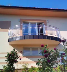 Balkon z nameščeno zaobljeno inox ograjo na stavbi z rumeno-oranžno fasado