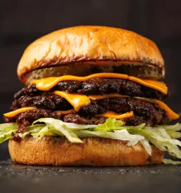 Klasičen smash burger, obogaten s svežo zeleno solato, plastjo topljenega čedar sira in izbrano omako, pripravljen za takojšnje uživanje.