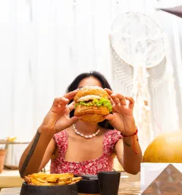 Ženska z veseljem uživa v sveže pripravljenem cheeseburgerju, kar pričara prijetno izkušnjo ob obisku dobre okrepčevalnice v Bovcu.