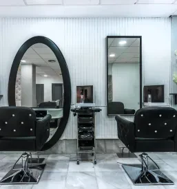 Svetel in minimalistično zasnovan frizerski salon s čisto notranjostjo, udobnimi stoli in modernim dekorjem, ki vabi stranke.