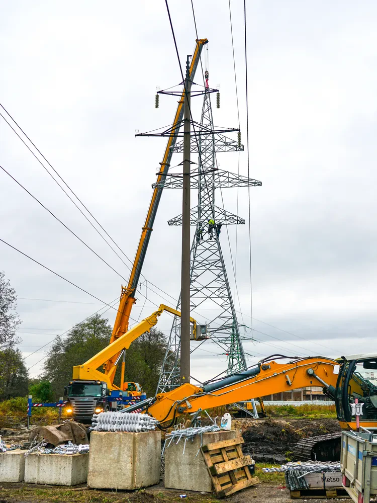 Delavci in žerjavi postavljajo daljnovod Skupina delavcev ob pomoči močnih žerjavov precizno namešča visokonapetostni daljnovod na gradbišču. Poudarek je na varnosti in inženirski natančnosti, ki je ključna pri tovrstnih industrijskih projektih.