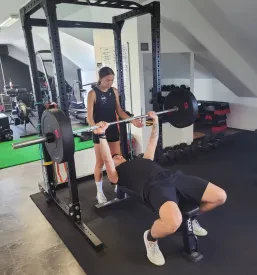 Član fitnesa pod nadzorom trenerja dviguje uteži  fitnesu.