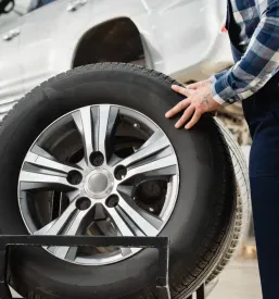 Mehanik v delovnih rokavicah odstranjuje kolo z avtomobila, dvignjenega na avtomobilskem dvigalu, kar kaže na strokovnost pri menjavi gum in Avtoservis in popravilo vozil Kisovec, Zagorje.