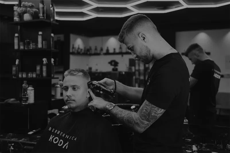 Natančno oblikovanje brade s škarjami Izkušen brivec s spretnimi rokami natančno oblikuje brado moškega s škarjami, poudarjajoč vsako podrobnost in stil za popoln videz.