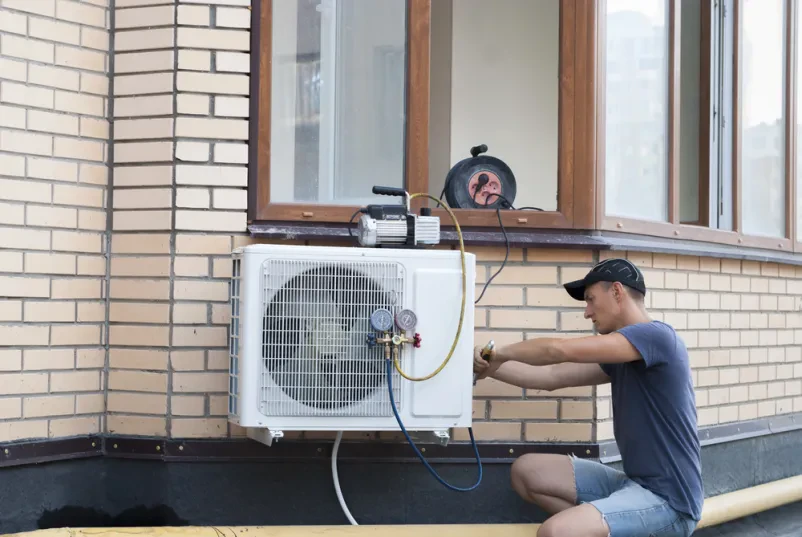 Delavec pritrjuje zunanjo enoto klimatske naprave na steno stanovanjske hiše, kar je ključni korak pri strokovni montaži novega sistema.
