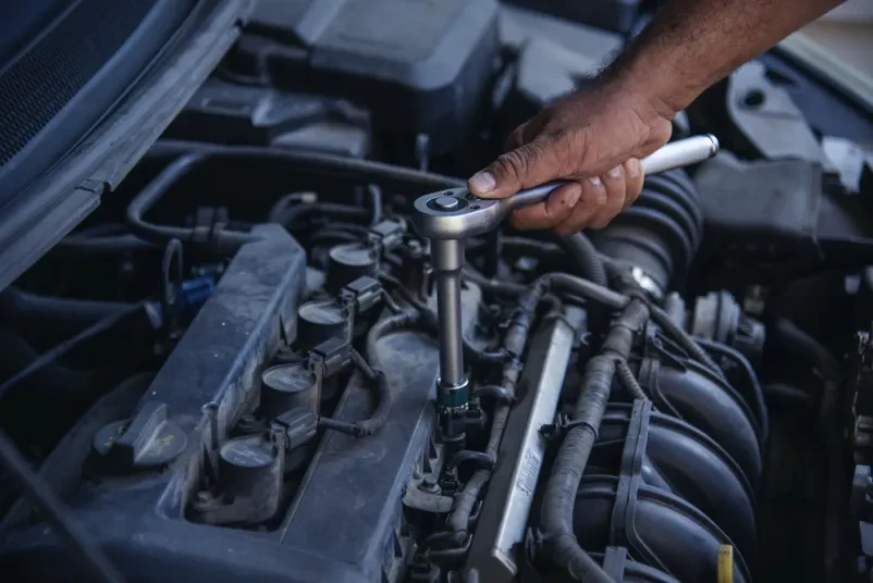 Popravilo motorja z orodjem Mehanik z orodjem popravlja motor avtomobila, ki ima odprt pokrov.
